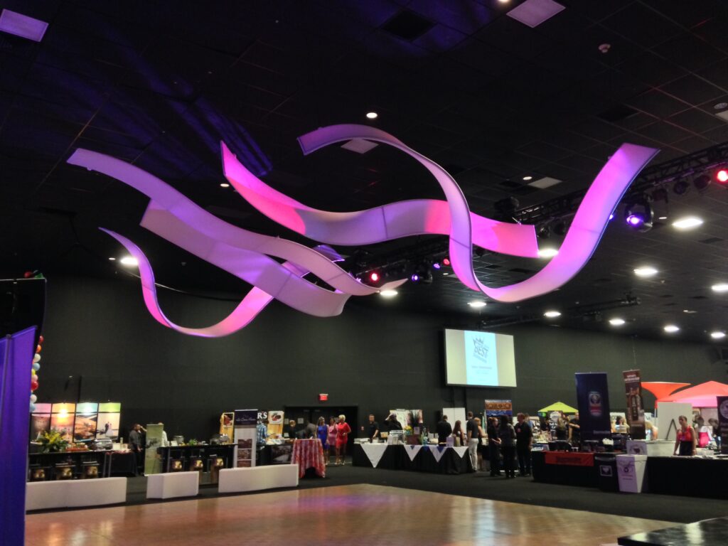 Look UP! These tension fabric ribbon structures are rental ceiling treatments suspended in your “otherwise uninvolved space.” For events, exhibits, and experiences the Originators AirWaves create an immersive environment